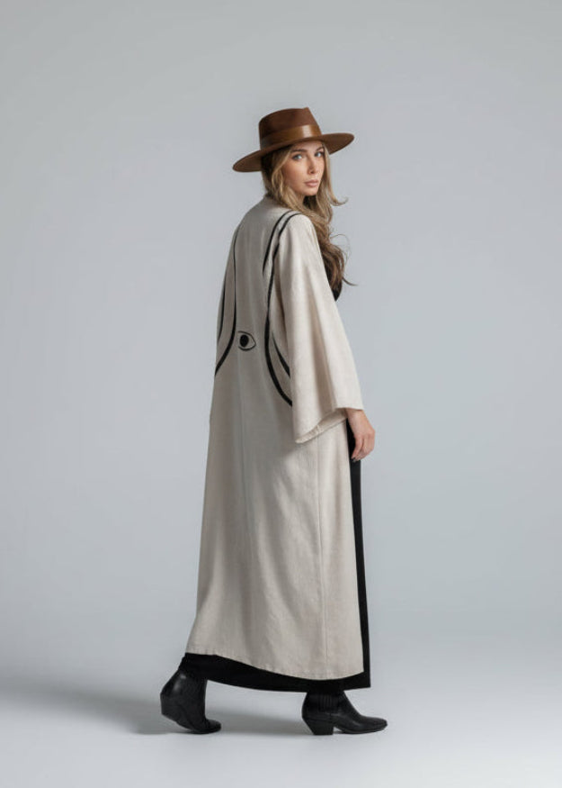 Woman wearing a long beige kimono layering piece with black hand-painted lines and evil eye motif